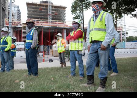 Austin, Texas USA 14 luglio 2020: I lavoratori del settore edile ascoltano le informazioni sulla sicurezza mentre si preparano per un turno di otto ore nel calore a 105 gradi del Texas. Gli equipaggi sono al secondo piano di un edificio a 53 piani, mentre prendono precauzioni contro la pandemia del coronavirus. Foto Stock