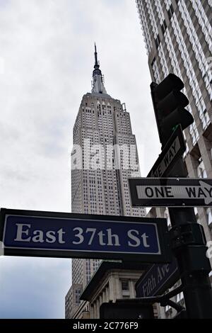 L'Empire state Building visto dietro i semafori, le indicazioni per East 37th Street e un cartello a senso unico. Un altro edificio sorge nell'angolo dell'immagine. Foto Stock