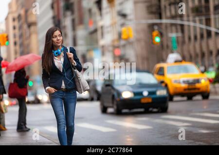 Giovane donna asiatica professionista che cammina a casa mentre si è in viaggio di lavoro in New York City Street. Gente urbana che commuter di stile di vita in giorno di pioggia di traffico di NYC Foto Stock