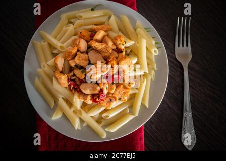Penne con pollo e verdure in salsa di pomodoro. Cucina mediterranea - un piatto di prodotti ecologici su un tovagliolo rosso su sfondo scuro Foto Stock