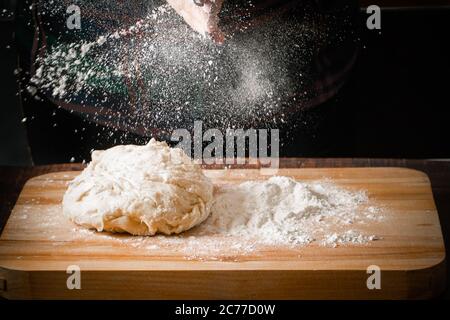 Farina che si versa dalle mani sull'impasto per pizza Foto Stock