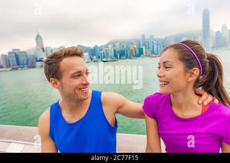 Felici coppie di corridori che vivono uno stile di vita sano attivo in forma nella città di Hong Kong ridendo insieme dopo aver eseguito l'allenamento all'aperto. Persone interrazziali felici Foto Stock