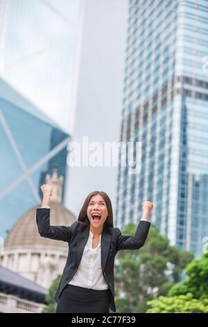 Donna di affari successo felice a Hong Kong che celebra il commercio riuscito con le armi in su le mani sollevate nell'aria che vince. Cinese multirazziale giovane Foto Stock