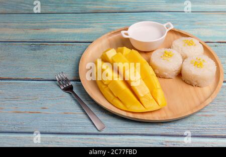 Mango giallo con forchetta piccola. Cubetti di frutta Mango sul tavolo di legno blu. Frutta tropicale asia. Buccia di mango gialla fresca e cubetti a fette su legno Foto Stock