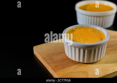 Primo piano creme brulee fatto in casa in ramekin bianco con zucchero di rabbocco su sfondo nero con spazio di copia. Creme brulee dessert francese Foto Stock