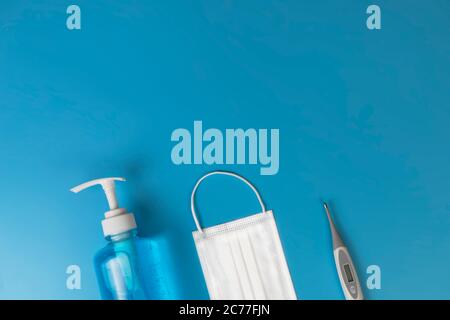Maschere igieniche termometro digitale, spray alcolico su fondo di mare blu. Maschera medica, disinfettante con alcol, termometro su sfondo blu con copia Foto Stock