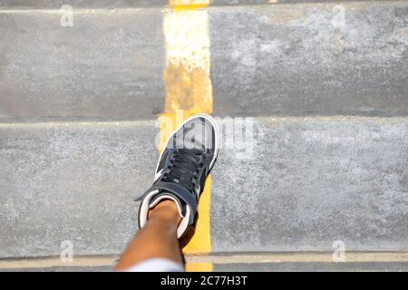 Gambe uomo con lunghe sneakers che camminano lungo scala pubblica con linea gialla in città. Foto Stock