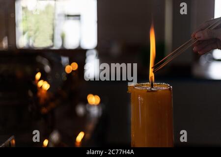 Concetto di Quaresima Buddista. Donne mano che illumina l'incenso da grandi candele nel tempio buddista primo piano forma di luce candele. Processo con stile chiave basso Foto Stock