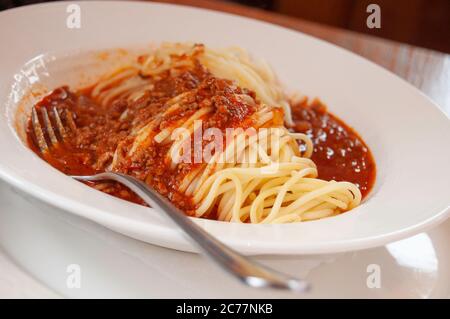 Un piatto bianco pieno di pasta bolognese, con un po' di salsa di pomodoro, immagine ravvicinata Foto Stock