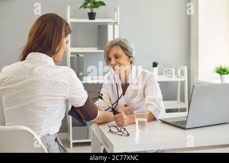 Medico senior che controlla la pressione sanguigna del paziente in ospedale. Giovane donna che consulta cardiologa in clinica Foto Stock