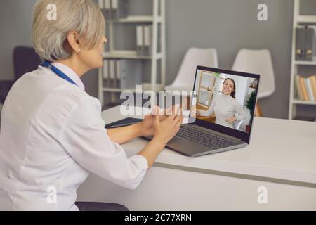 Medico senior in video chat con i giovani pazienti in ospedale. Medic parla con il cliente sul computer portatile dal suo ufficio Foto Stock