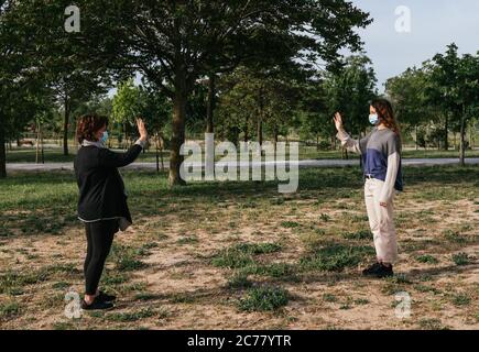 Distanza sociale. Due vicini camminano attraverso un parco e si salutano mentre mantengono la loro distanza dalla pandemia. Pandemia. Dispositivi coronavirus. Foto Stock