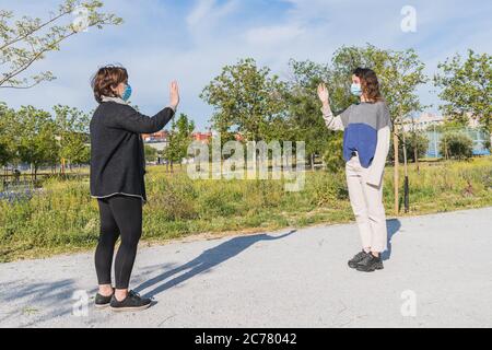 Distanza sociale. Due vicini camminano attraverso un parco e si salutano mentre mantengono la loro distanza dalla pandemia. Pandemia. Dispositivi coronavirus. Foto Stock