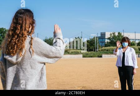 Distanza sociale. Due vicini camminano attraverso un parco e si salutano mentre mantengono la loro distanza dalla pandemia. Pandemia. Dev. Virus coronazione Foto Stock