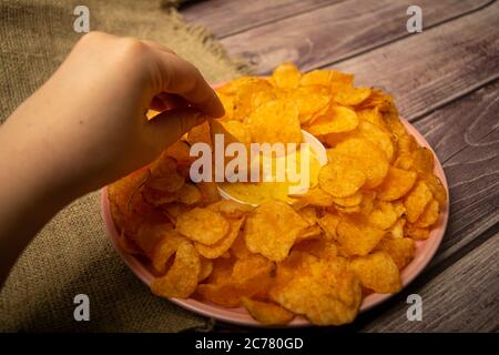 La ragazza prende un chip da un piatto rotondo con patatine e una pentola con salsa di formaggio al centro del piatto. Primo piano Foto Stock