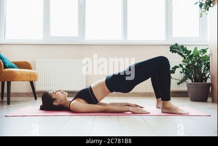 Donna caucasica che indossa abbigliamento sportivo facendo esercizi di abs sul pavimento a casa durante il blocco Foto Stock