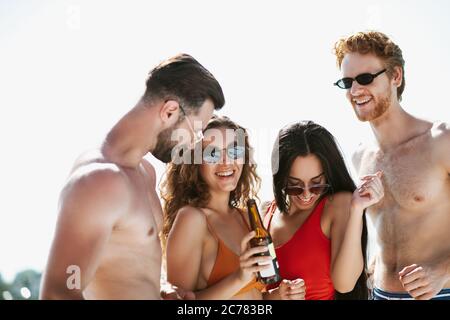 Giovani in costume da bagno che hanno tempo a bere birra, sensazione di flirtezza Foto Stock