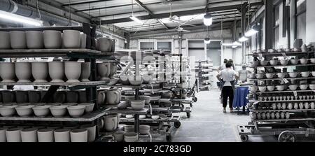 Boleslawiec, bassa Slesia, Polonia., scaffali in un'affollato studio di ceramica pieno di lavori finiti e pezzi di argilla che asciugano sotto il controllo di una donna Foto Stock