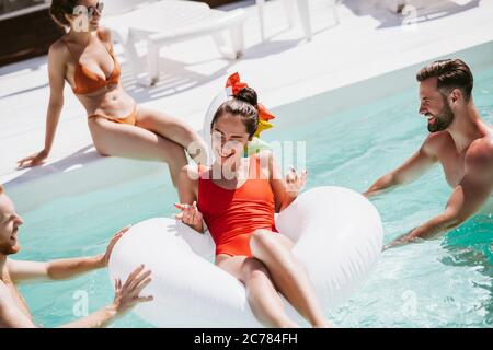 Bella donna dai capelli scuri in un costume da bagno rosso che dfrifting su un anello da nuoto in piscina Foto Stock