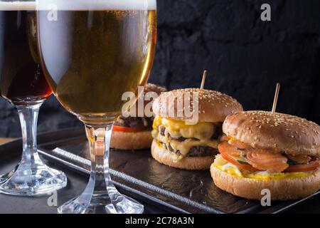 primo piano, bicchieri da birra con birra artigianale scura e chiara con schiuma, sullo sfondo di hamburger, con una varietà di ingredienti, tra cui lo shyomga Foto Stock