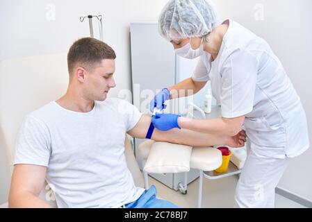 l'uomo in ufficio medico dà sangue. medico mette il laccio sul braccio Foto Stock