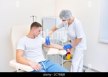 l'uomo in ufficio medico dà sangue. medico mette il laccio sul braccio Foto Stock