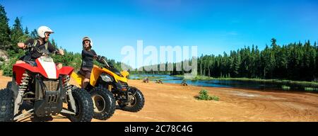 Quad ATV guida persone. Felice coppia sorridente ciclisti sulla spiaggia presso il bellissimo lago. Foy, lago Foyross, Sudbury, Ontario, Canada. Foto Stock