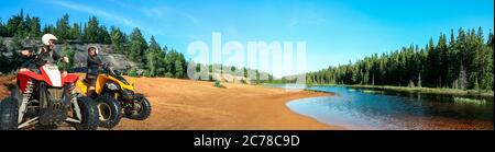 Quad ATV guida persone. Felice coppia sorridente ciclisti sulla spiaggia presso il bellissimo lago. Foy, lago Foyross, Sudbury, Ontario, Canada. Foto Stock