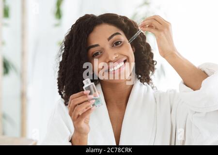 Concetto di cura della pelle. Bottiglia da donna africana sorridente con siero idratante Foto Stock