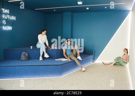 Gruppo di studenti moderni multietnici seduti nella hall del campus e in preparazione all'esame Foto Stock