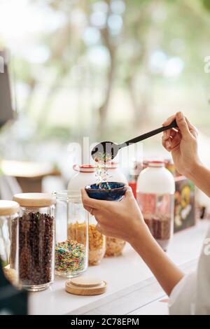 Mano del cameriere mettendo un cucchiaio grande di spruzzette in ciotola con gelato per il cliente Foto Stock