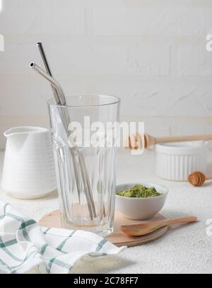 Fuoco selettivo, tè caldo matcha, latte, in vetro ad alta trasparenza e tubi metallici, con latte, in un interno domestico con piatti bianchi Foto Stock