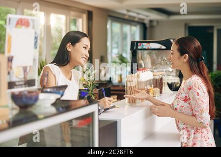 Bella giovane donna asiatica talkig al barista e ordinare caffè e dessert Foto Stock