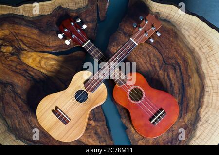 Due ukulele in colori diversi - marrone chiaro e scuro su un bel tavolo di legno. Foto Stock