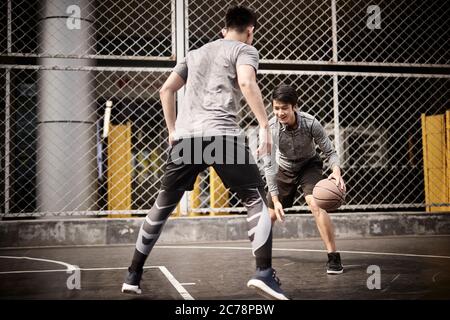 due giovani uomini adulti asiatici che giocano a basket uno a uno sul campo all'aperto Foto Stock