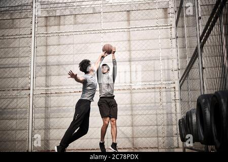 due giovani uomini adulti asiatici che giocano a basket uno a uno sul campo all'aperto Foto Stock