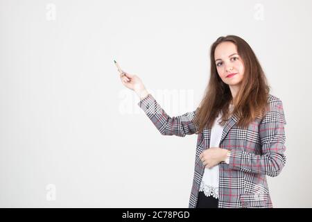 bella giovane donna in abiti formali di affari si pone contro una parete bianca e punta a qualcosa Foto Stock