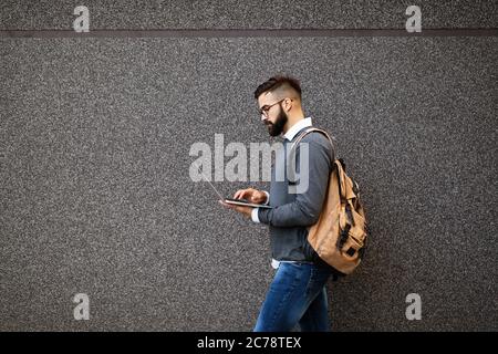 Uomo d'affari a piedi in strada tenendo il suo portatile, lavorando all'aperto Foto Stock