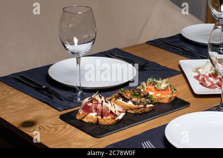 Tre bruschette di pane affettato, funghi, salmone e carne su un tavolo di legno nel ristorante. Spuntini e panini Foto Stock