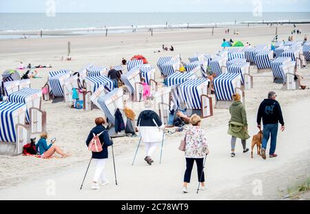 15 luglio 2020, bassa Sassonia, Norderney: I turisti camminano di fronte alle sedie da spiaggia sulla passeggiata sulla spiaggia settentrionale dell'isola. Oggi, mercoledì è l'ultimo giorno di scuola prima delle vacanze estive di sei settimane per gli alunni della bassa Sassonia. Foto: Hauke-Christian Dittrich/dpa Foto Stock
