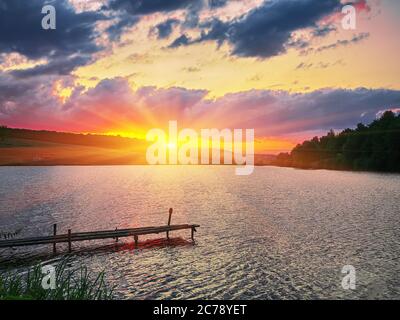 Molo in legno, molo, su un lago di sera. Tramonto spettacolare Foto Stock