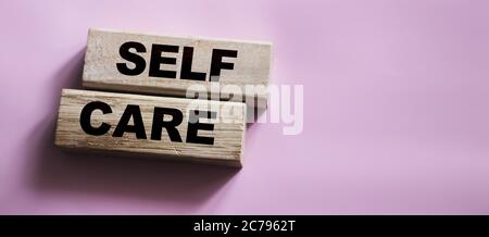 Parole di cura su blocchi di legno, concetto di trattamento autonomo, sfondo rosa Foto Stock