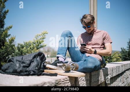 Uomo felice che giace su recinzione e che usa lo smartphone Foto Stock