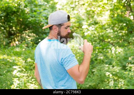 Ogni SIP conta. Ragazzo maturo in cappello. Viaggiatore hipster assetato. Acqua potabile nella foresta all'aperto con tramonto natura sullo sfondo. Uomo bearded con bottiglia d'acqua. Ritratto di fitness dell'uomo bearded. Foto Stock