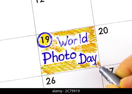 Dita donna con penna che scrive promemoria Giornata Mondiale della Foto in calendario. Agosto 19. Foto Stock