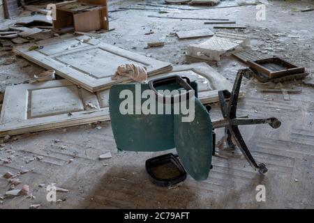 Sporco bussato sopra la sedia girevole dell'ufficio in un pavimento disordinato della stanza dell'edificio abbandonato Foto Stock