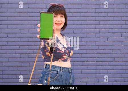 Giovane donna caucasica che mostra il suo smartphone con chiave cromatica alla fotocamera. Concetto di prevenzione del coronavirus. Foto Stock