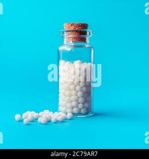 Immagine ravvicinata di globuli omeopatici in bottiglia di vetro su sfondo blu pastello. Medicina alternativa erbe, sanità e concetto di pillole omeopatia. Foto Stock