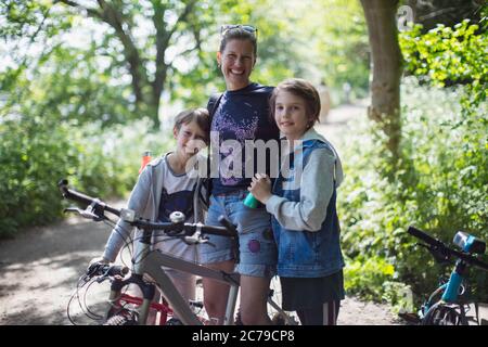 Ritratto felice madre e figli godendo di giro in bicicletta nel parco soleggiato Foto Stock