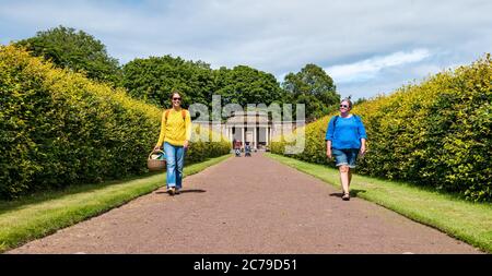 Haddington, East Lothian, Scozia, Regno Unito, 15th luglio 2020. Amisfield Walled Garden riapre: Giardino del 18th ° secolo, uno dei più grandi in Scozia. E 'ora aperto 3 giorni alla settimana con un sistema di prenotazione online dopo le restrizioni di blocco attenuati durante la pandemia di Covid-19. Kate e Claire portano un pic-nic a piedi lungo un ampio sentiero che conduce lontano dalla struttura ad angolo fiancheggiata da siepi nel sole estivo Foto Stock